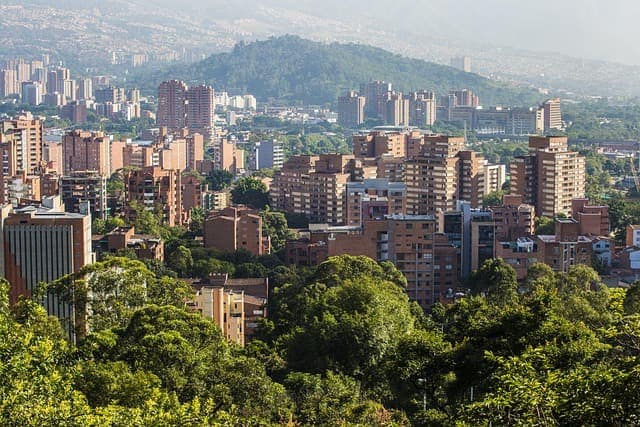Apartment towers of a Colombian city among green trees, with a forested hill behind