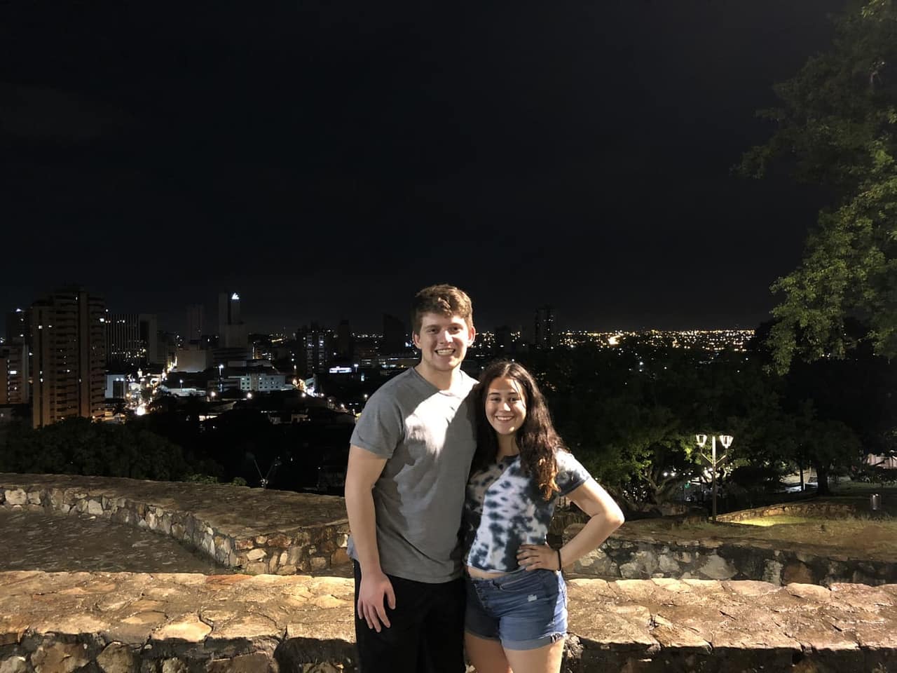 Sthephany and Seth at a stone lookout in Colombia with the city lights glowing behind them at night