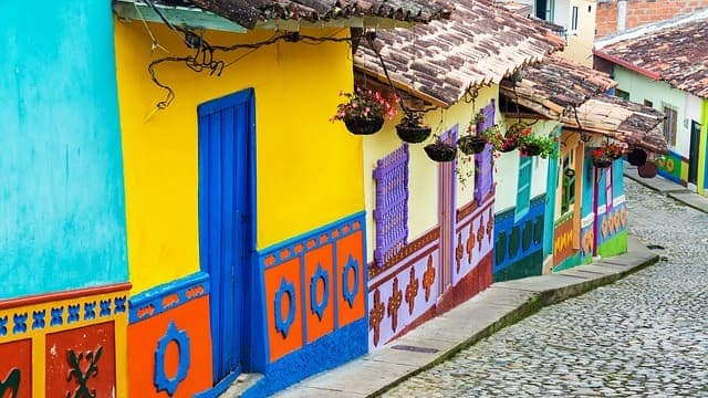Brightly painted yellow, blue, and orange houses with flower pots along a cobblestone street in Colombia