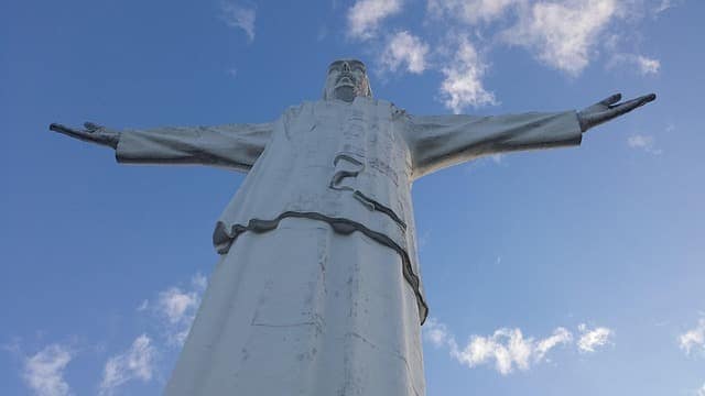 The Cristo Rey statue with arms outstretched, seen from below against a blue sky